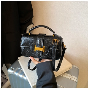 Detail of black glossy crinkled leather handbag with gold buckle and adjustable strap
