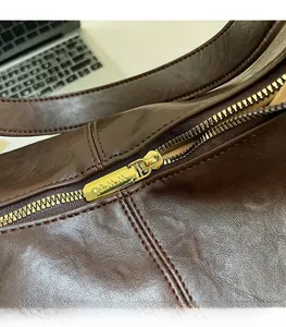 Detail of smooth gold zipper slider and textured dark brown leather on bucket bag