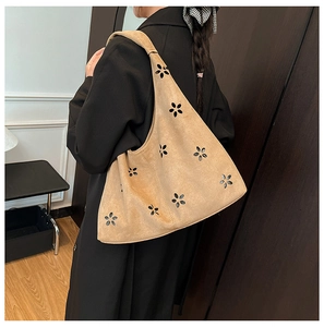 Detail of laser-cut floral patterns on a camel suede tote bag worn by a model