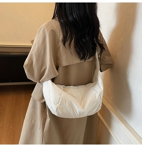 Detailed view of white padded nylon crescent crossbody bag worn with a casual coat