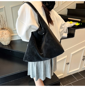Detail of black suede tote bag with white stitching and minimalist branding on shoulder