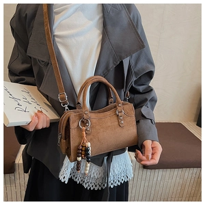 Détail du sac à main en daim marron avec rivets argentés et pompon en perles de bois