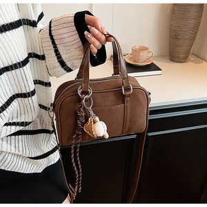 Detailed close-up of brown suede Boston bag with baseball glove charms and braided rope