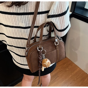 Detail view of a dark brown suede bowling bag with a cute mushroom charm and woven rope