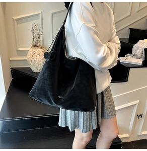 Detail view of large black suede tote bag with white stitching and minimal logo