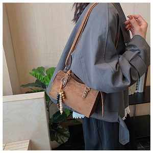 Petit sac carré marron en daim mat avec pompon en perles porté à l'épaule par un modèle