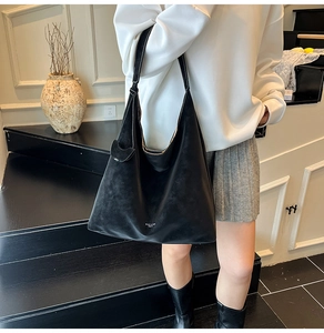 Detailed view of black matte leather tote bag with white lettering and long shoulder strap