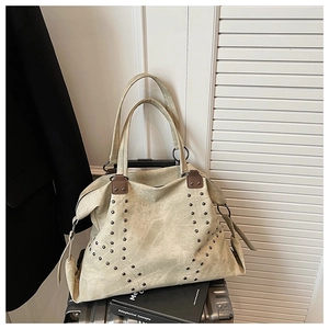 Detail of beige tote bag featuring metallic rivets and vintage buckle on a suitcase