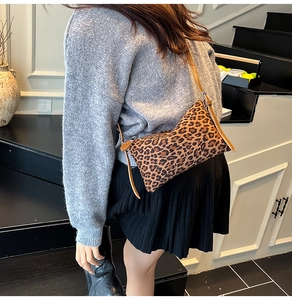 Close-up of leopard print crossbody bag with brown strap worn over a grey sweater