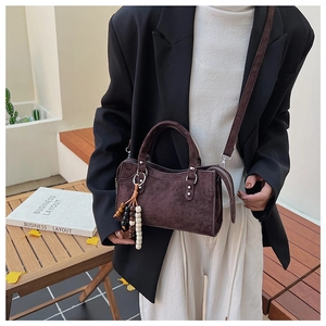 Détail du sac bandoulière en daim marron foncé avec breloque perlée et fine lanière