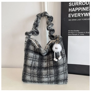 Détail d'un sac cabas en peluche à carreaux gris avec poignées plissées et breloque poupée