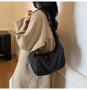 Side view of black nylon hobo bag worn with a beige trench coat for a casual look