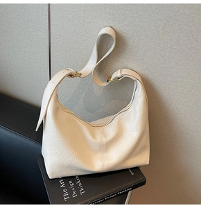 Close-up of cream soft leather hobo bag with adjustable gold buckle on black book prop