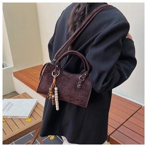 Détail du sac Boston en daim marron foncé avec pompons vintage et breloque en bois