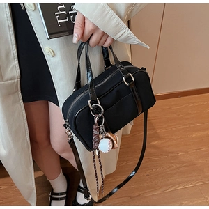 Detail of black Boston bag with baseball charm and patent leather handles for women