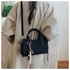 Détail du sac bandoulière vintage noir mat avec perles en bois sur un trench-coat beige