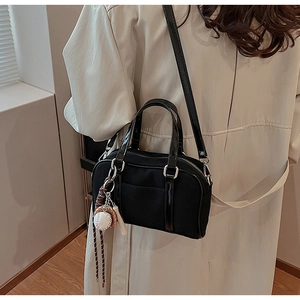 Boston bag with glossy handles and baseball charm worn by a model in a trench coat