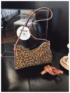 Close-up of leopard print baguette bag with brown leather straps and vintage vinyl background