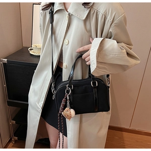 Detail of a black Boston bag with nylon body, shiny leather handles, and baseball charm
