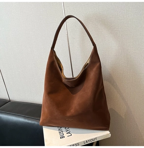 Detail shot of a dark brown suede hobo bag with a gold logo and wide shoulder strap