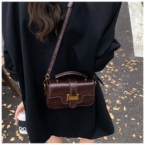 Street style shot of a dark brown patent leather handbag with a gold H-shaped metal buckle