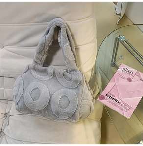 Close-up of grey plush tote bag with circular pattern on soft textured sofa