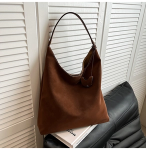 Detail of a deep brown suede tote bag with heart charm against a white window blind