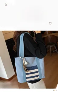 Detail of light blue canvas tote bag with striped pocket and fluffy pompom charm