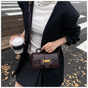 Detail of dark brown vintage crossbody bag with glossy texture and golden H-shaped clasp