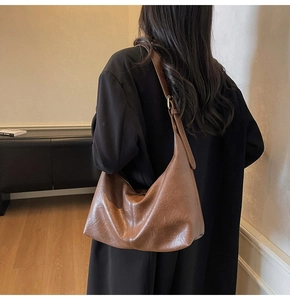 Close-up of vintage brown leather hobo bag with adjustable strap on a black blazer