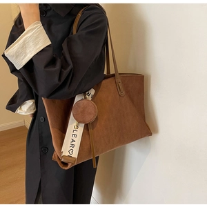 Detail of a brown tote bag featuring a decorative woven strap and small round purse pendant