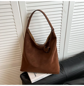 Detail of brown suede tote bag with leather strap and heart charm on a leather sofa