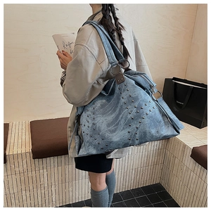 Detail view of large light blue denim tote bag with vintage metal rivets on shoulder strap