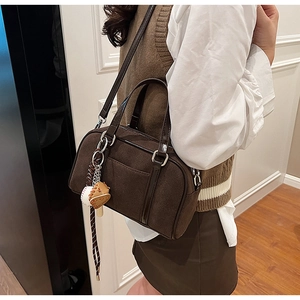 Detail of dark brown suede bowling bag with decorative baseball glove charm and leather strap