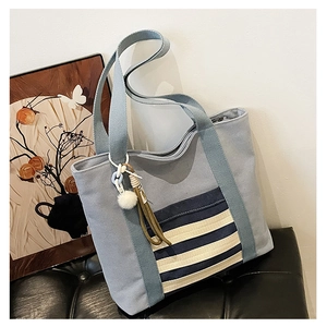 Close-up of grey-blue canvas tote bag featuring striped pocket and plush pompom tassel
