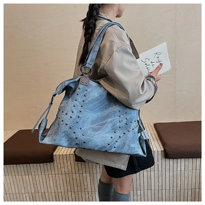 Close-up of light blue denim tote bag with silver studs and metal ring buckle detail