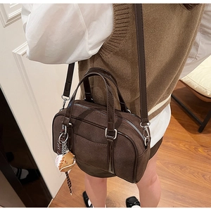 Detail of dark brown matte suede shoulder bag with glossy trim and baseball charm