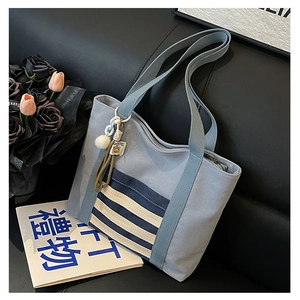 Detail of blue canvas tote bag featuring a striped front pocket and fuzzy ball charm