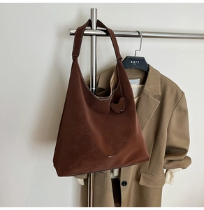 Detail view of a large brown suede tote bag hanging next to a blazer for commuting