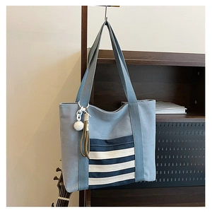 Detail of light blue canvas tote with navy stripe pocket and fuzzy ball charm hanging