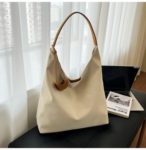 Detail of a minimalist cream tote bag with brown shoulder strap and heart charm on a bench