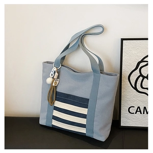 Close-up of light blue canvas tote bag with striped pocket and plush charm on black table