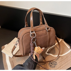 Detail of brown suede Boston bag with leather trim and colorful woven pendant strap