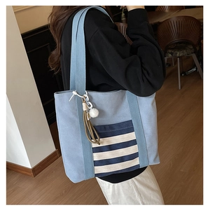 Detail view of light blue canvas tote bag featuring navy striped pocket and decorative charm