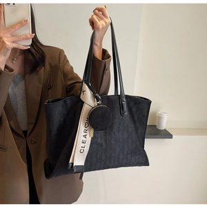 Detail of black tote bag featuring textured suede finish and a circular coin purse charm