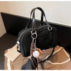 Detail of black Boston bag featuring creative baseball charm and glossy leather trim