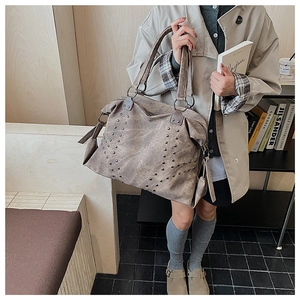 Chic taupe faux leather tote bag with V-shaped metal studs shown in a cozy home setting