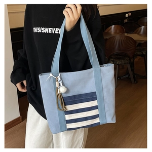 Detail of light blue canvas tote bag with navy striped pocket and white pom-pom charm