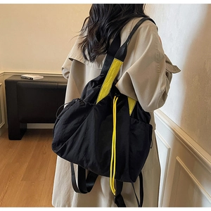 Detail of black nylon multi-functional backpack with neon yellow straps worn on a trench coat