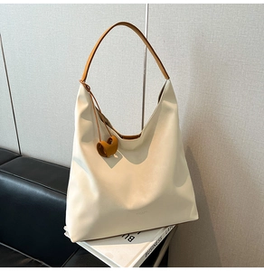 Detail of cream tote bag with brown handles and heart charm on a stack of books